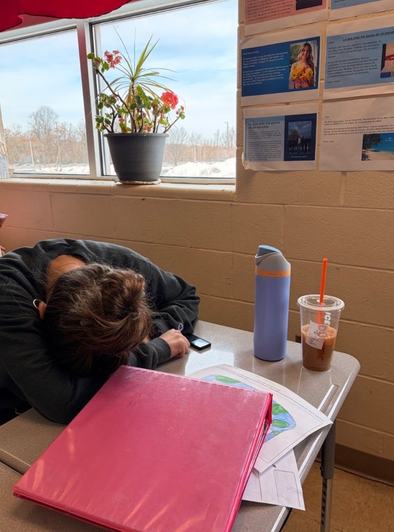 A tired Neshaminy High School student wears earpods while she takes a nap surrounded by her iced coffee and papers on Mar. 2, 2026, in Lang., Pa. The girl got little sleep after staying up to complete her homework. (The Playwickian / Megan Rubbo)